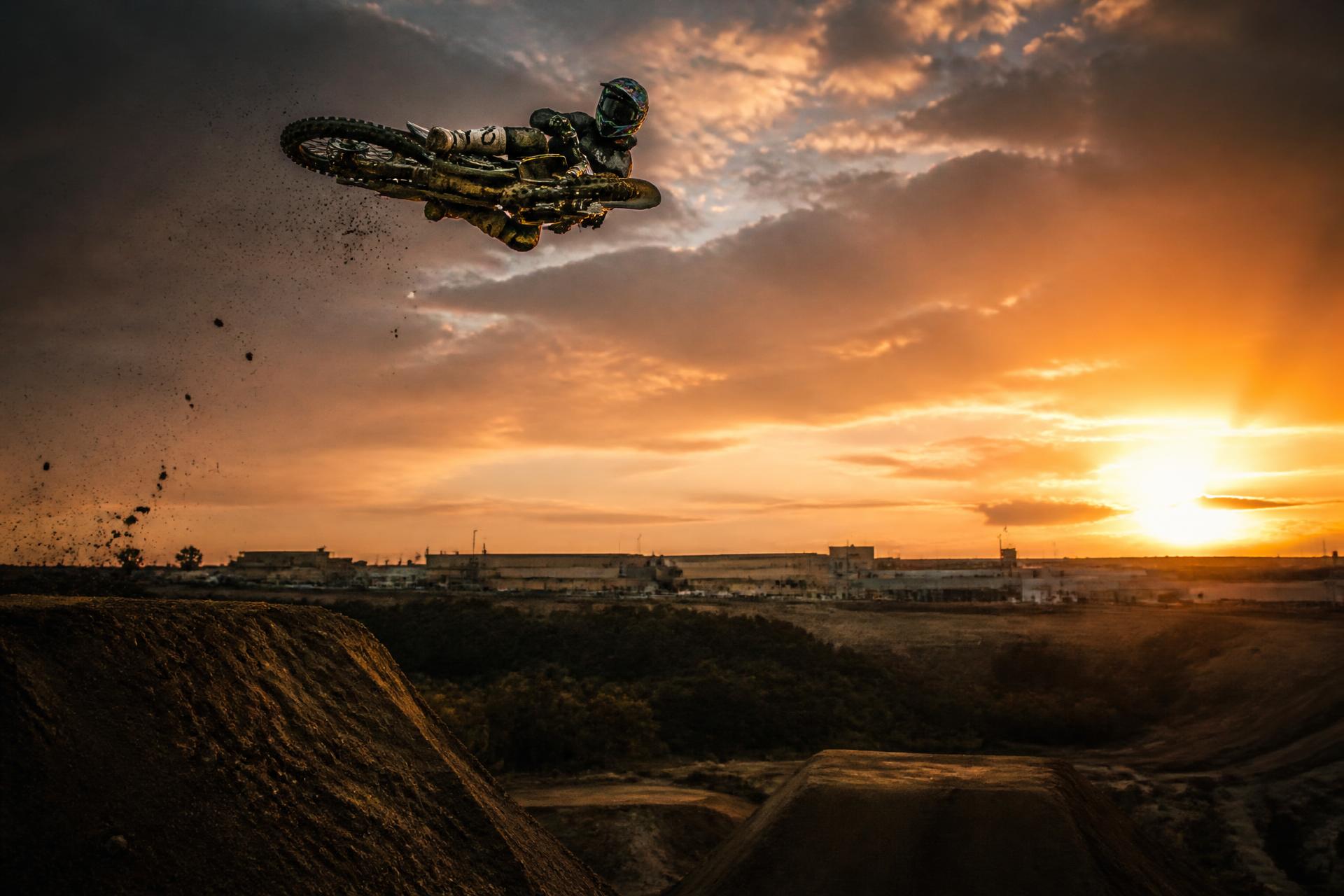 Freestyle motocross rider laying the bike out sideways in a whip against a burning sunset