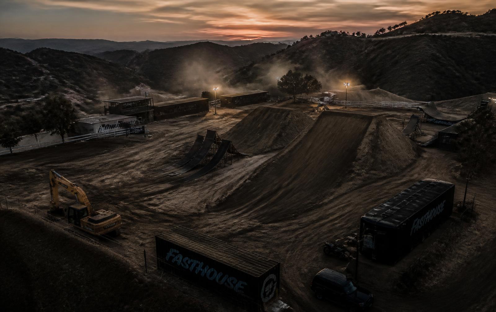 Aerial view of the private freestyle motocross compound at dusk — ramps, landings and shipping containers ringed by hills